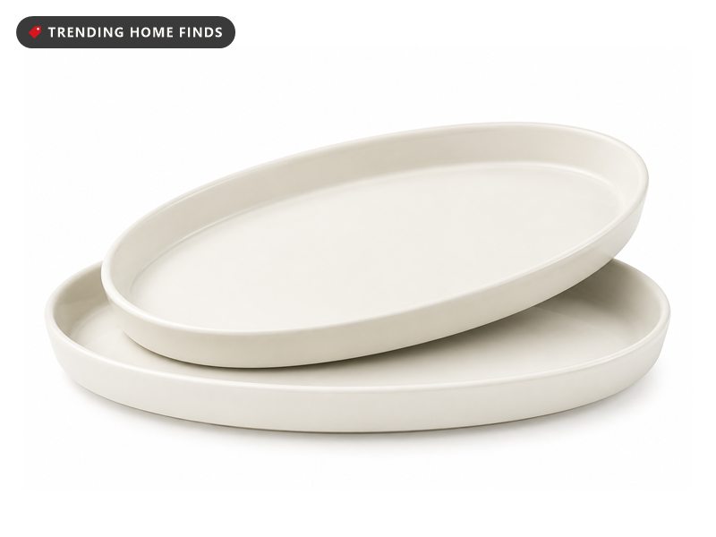 Two large creamy white oval porcelain platters with deep rolled rims, one resting at an angle on the other.