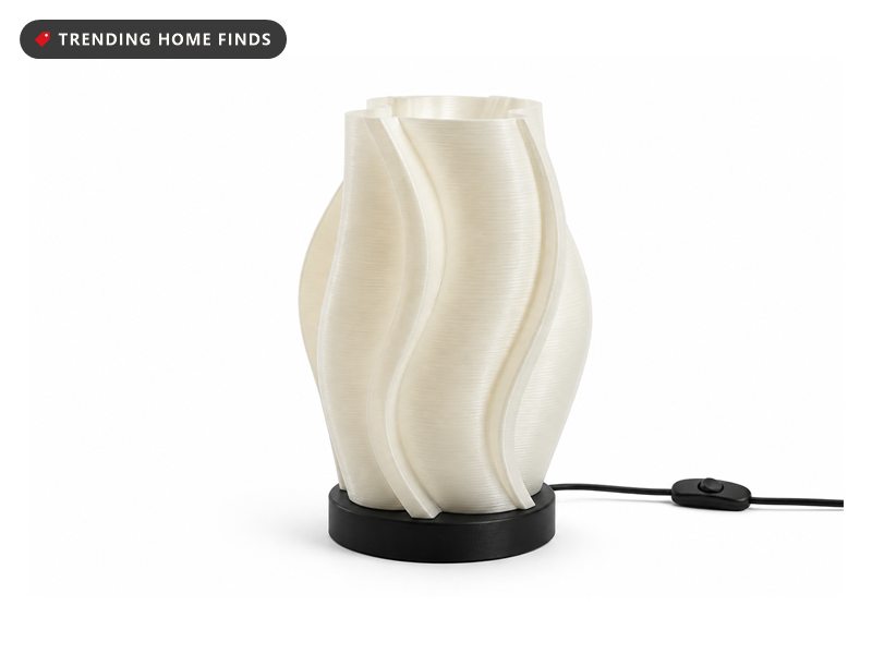 A ribbed 3D-printed lamp on a bedroom nightstand throwing a fanned pattern of light and shadow up the wall before dawn.