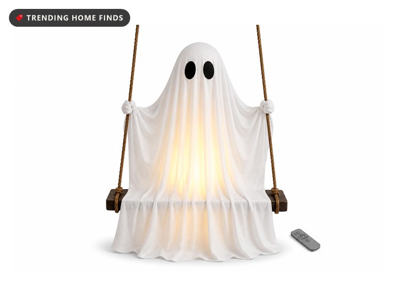 Five foot white draped ghost with two black oval eyes, lit from inside, hanging on ropes above a dark wooden swing seat.