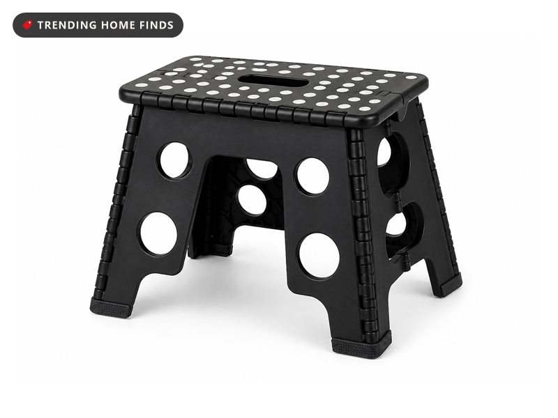 A black folding step stool with white non slip dots on the platform, standing open on a wood floor.