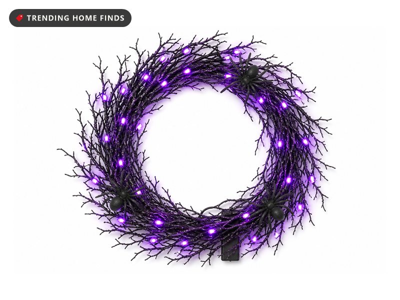 Round black glitter twig wreath lit with small purple bulbs, three black plastic spiders sitting in the branches.