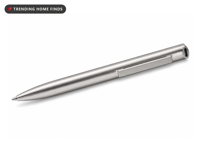 A slim aluminum recorder pen resting beside an open notebook and a coffee cup on a dark walnut desk late at night, lit by one small lamp.