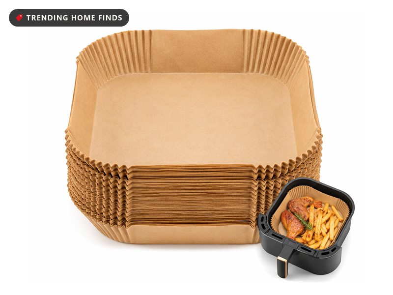 Tall stack of square unbleached parchment air fryer liners beside a black air fryer basket lined with one and filled with fries