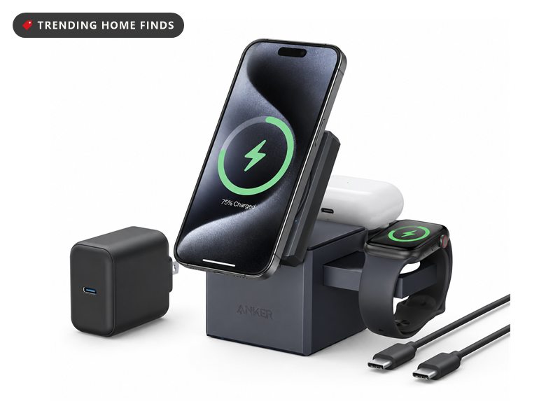 Anker charging cube holding a phone upright while a smartwatch and earbuds case charge on its base