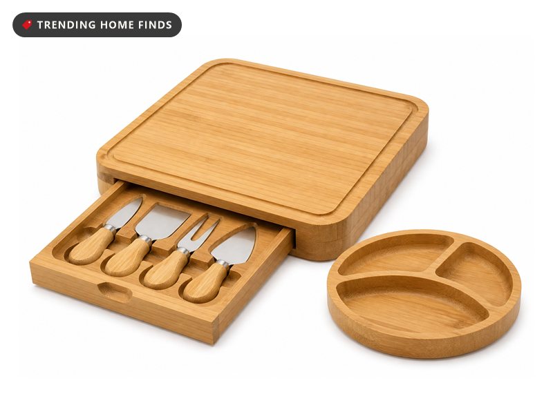 Round bamboo charcuterie board with a slide-out drawer holding four cheese knives, loaded with cheese, grapes and crackers