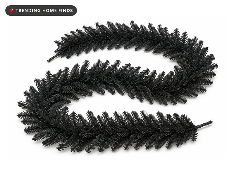 Two lengths of matte black faux pine garland laid in a long curve, needles fanning out along a flexible spine.