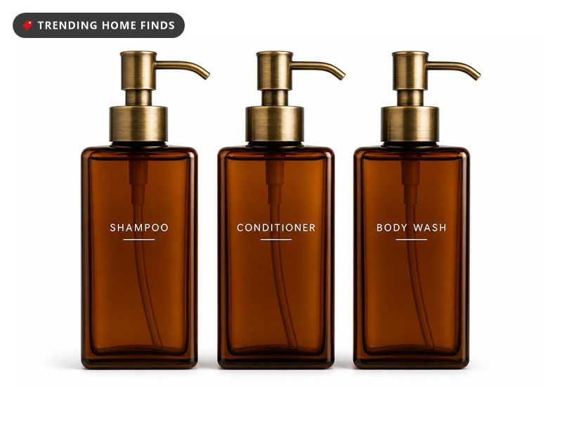 Three amber glass pump bottles with brushed gold pumps, labelled shampoo, conditioner and body wash.