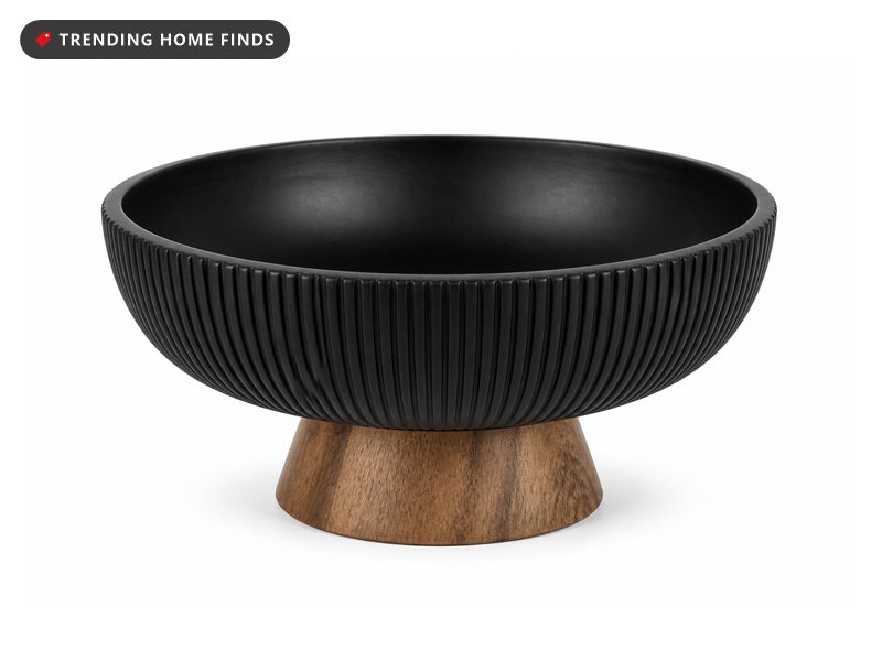 A shallow black carved mango wood bowl with a fluted rim standing on a natural wood pedestal foot.