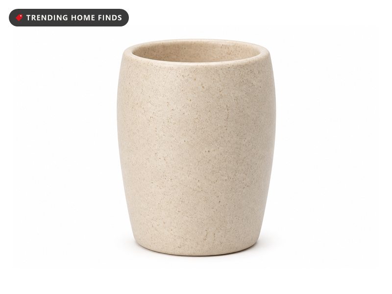 A speckled matte beige ceramic toothbrush holder, a tapered cylinder with a plain level rim.