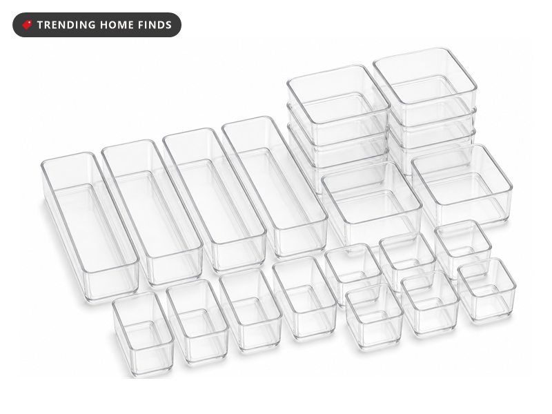 Twenty five clear plastic drawer organizer trays in four sizes, some stacked empty and some holding makeup brushes, skincare bottles and jewelry