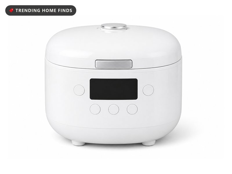 White CUCKOO Micom rice cooker with a digital clock display and preset buttons on the front, on a counter beside a bowl of cooked rice and a rice paddle