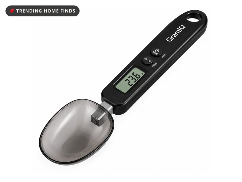 Black digital weighing spoon with a stainless steel bowl and a small lit display reading 23.6 grams