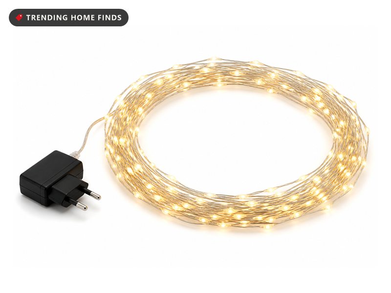 A long coil of thin silver copper wire set with tiny warm white LED points, lit, with a small black plug adapter.