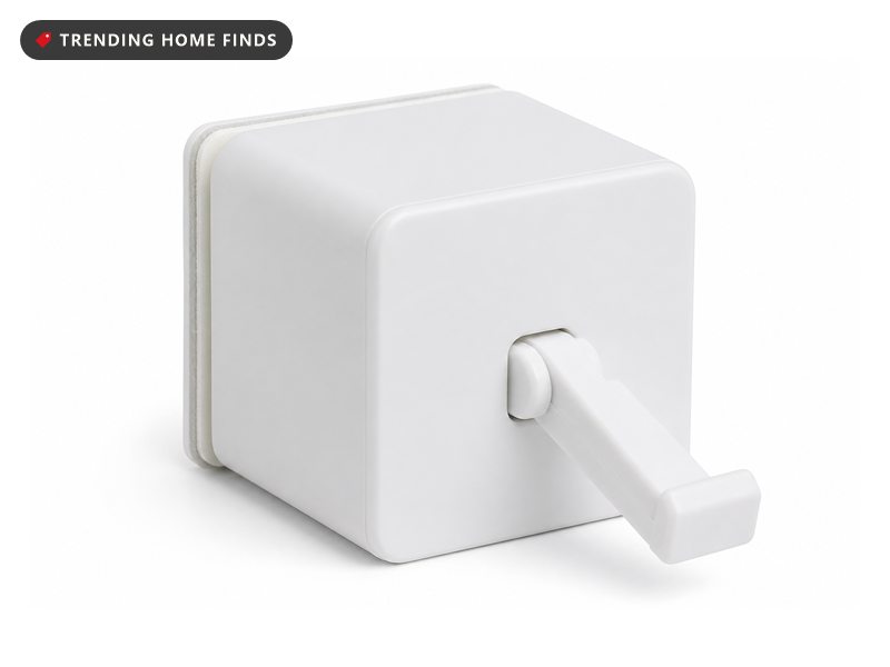 A small white cube stuck beside the power switch of a coffee maker on a rental kitchen counter, its arm pressing the switch down in flat daylight.