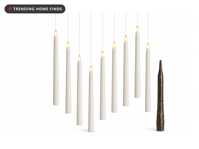 White taper candles with warm flickering tips hanging on clear line at staggered heights above a dark table.