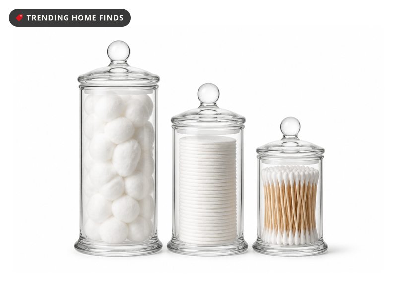 Three clear glass apothecary jars in graduated sizes with domed lids and round glass knobs, filled with cotton.