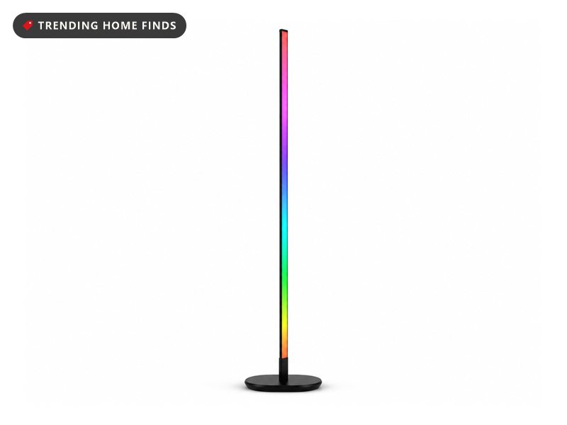 Slim black corner floor lamp standing on a small round base, its front face lit in a rainbow gradient