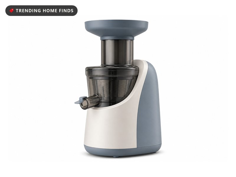 Stone blue cold press slow juicer with juice in its pitcher and a stack of oranges beside it on a white background.