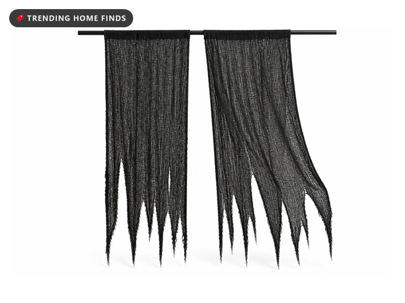 Two long panels of torn black gauze hanging from a straight rod, their lower edges cut into ragged tongues.