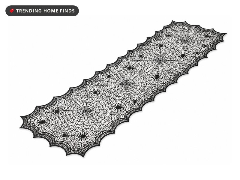A black lace runner knitted through with a spider web pattern and scalloped web edges, laid down a wooden table.