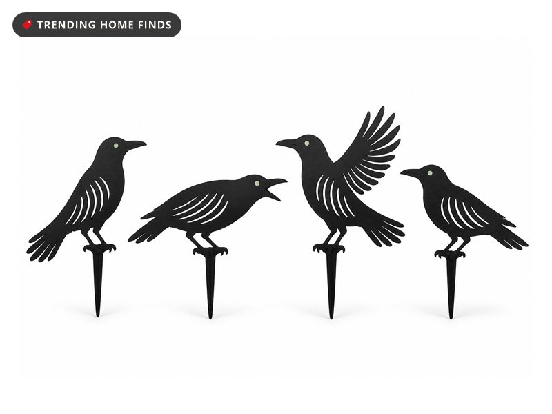 Four flat black metal crow silhouettes on ground stakes, each cut with a skeleton rib pattern and a small pale green eye.