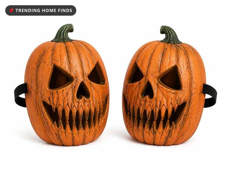 Two orange carved pumpkin skull shells with hollow eye sockets and long ridged teeth, open at the back with a black elastic strap.