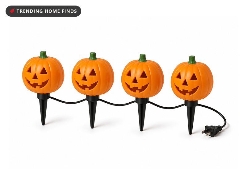 Four molded orange jack o lantern lights on short black ground spikes, linked in a row by one thin black cord.