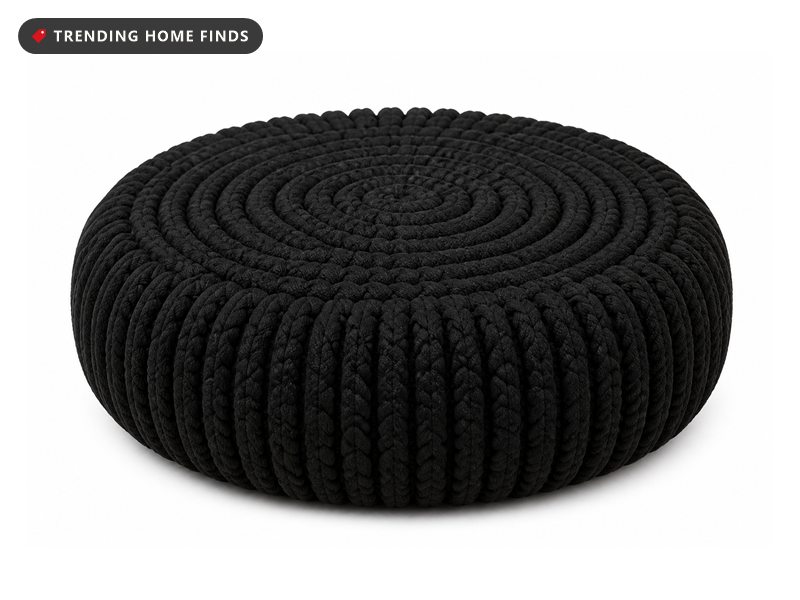 A round black pouf hand knitted from thick cotton rope in a spiral rib, with a flat top and softly rounded sides.