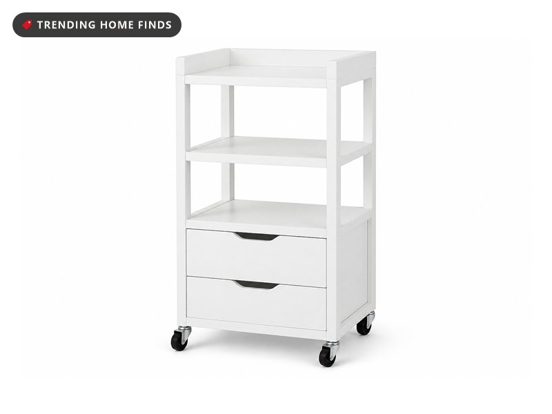 Narrow white rolling makeup and skincare cart with open shelves and two drawers, on a white background.