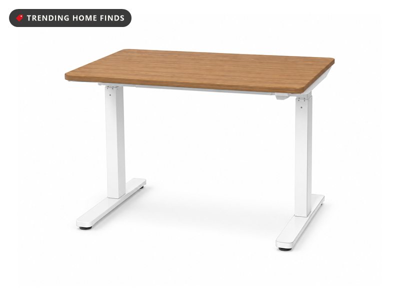 Small electric standing desk with a light walnut top on a white two-leg frame