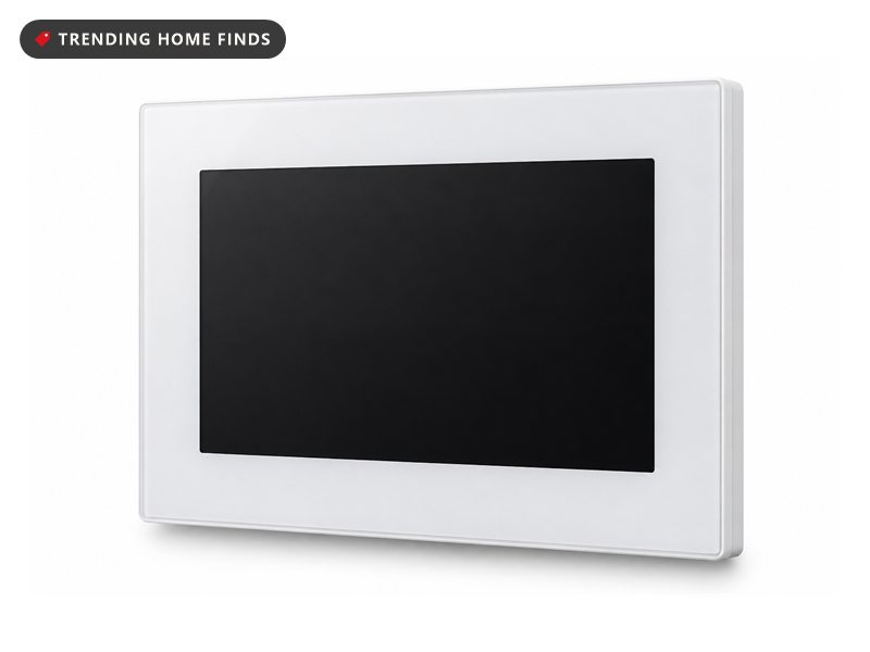 A five-inch white touchscreen control panel set flush into a hallway wall beside framed art, golden hour light raking across the entryway.