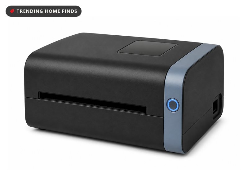 Low black desktop thermal label printer with a wide front output slot, a round button on the right end and a pale gray trim band.