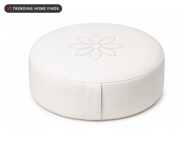 A round white meditation cushion with a gray flower outline stitched on top.