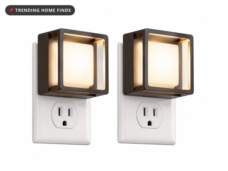 Square black-framed plug-in night light glowing warm white on an outlet