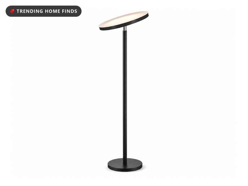 Minimal black torchiere floor lamp with a flat tilted disc head glowing warm white