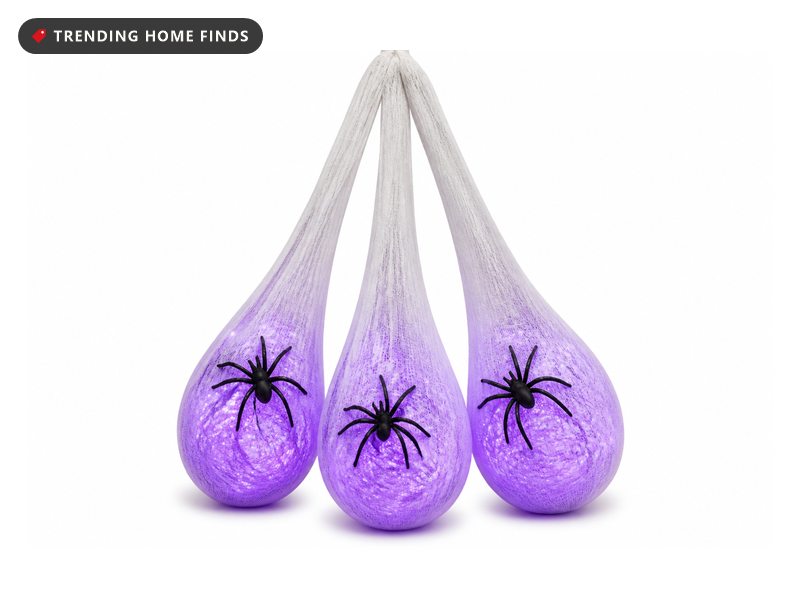 Three hanging gauze egg sacs lit purple from inside with a black spider clinging to each one.