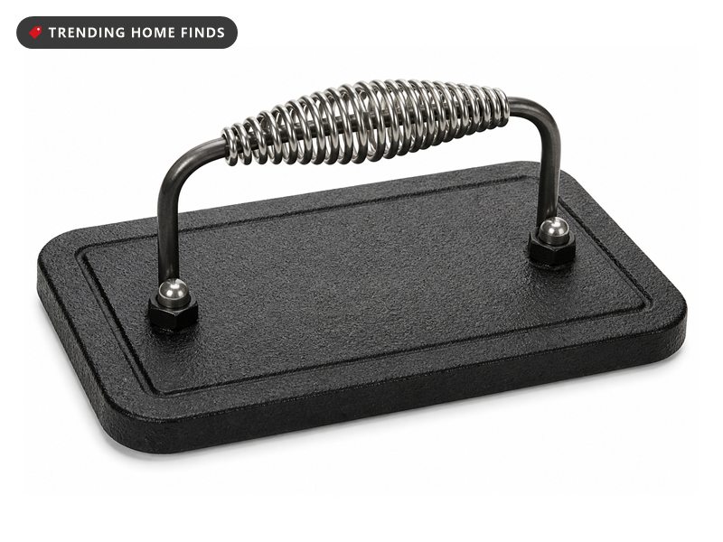 Rectangular black cast iron grill press with a pebbled surface and an arched steel handle with a coiled grip.