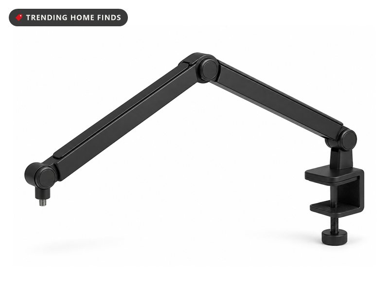 Black low profile mic arm curving up from beneath the monitor on a streaming desk setup, microphone floating at chin height in bright midday light.