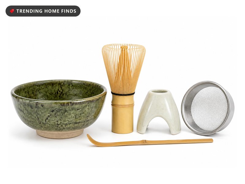 A mottled green bowl and bamboo whisk mid-froth on a pale kitchen shelf before dawn, a small matcha bar at home laid out on linen.