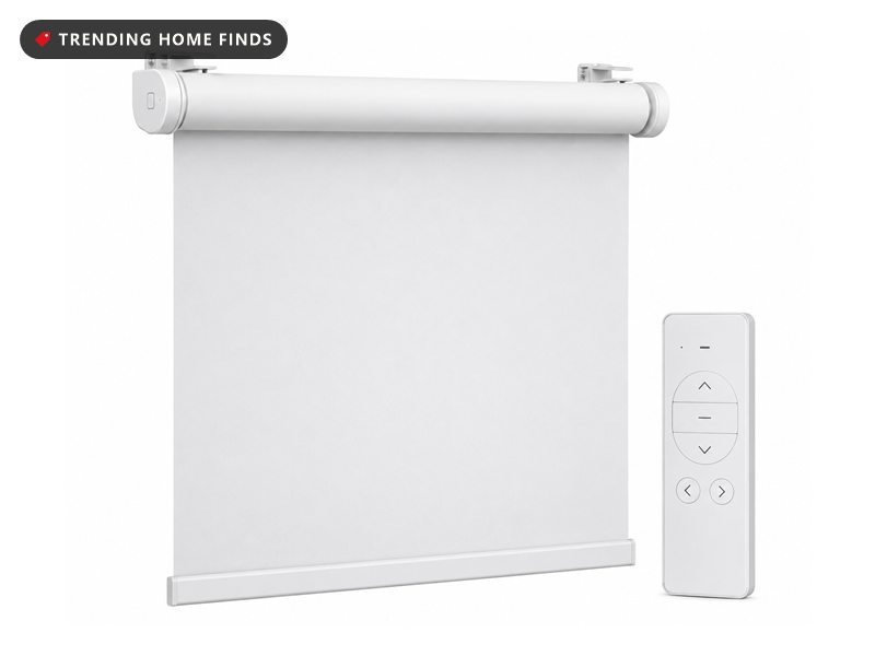 White cordless motorized roller blind partly lowered on its bracket, shown with its handheld remote