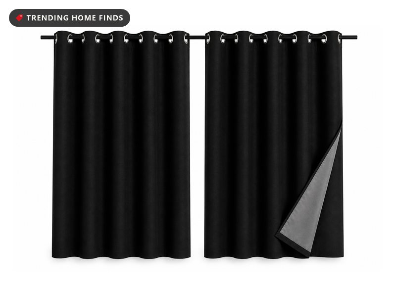 Two matte black curtain panels hanging in soft folds from silver grommets, the right one folded back to show a pale lining.