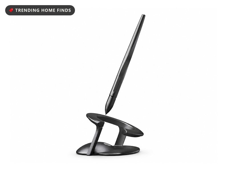 Slim dark gunmetal pen balanced tip-down at a steep angle on a sculpted metal stand, on a white background