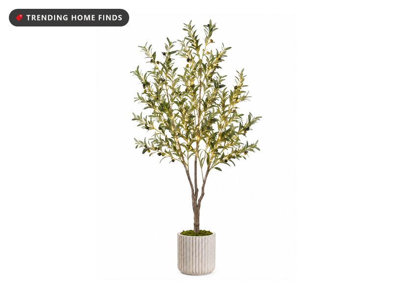 Six-foot artificial olive tree with green leaves, small olives and warm string lights woven through the branches, planted in a ribbed cream stone pot