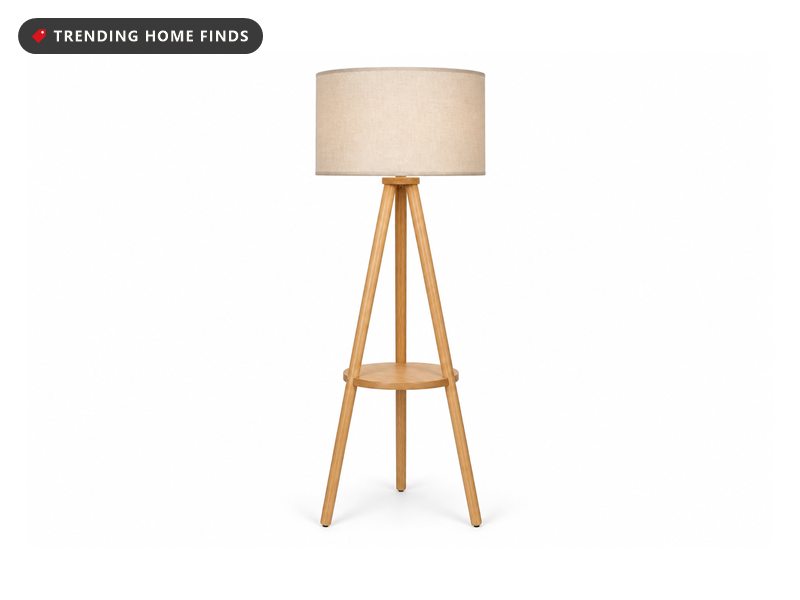 Wood tripod floor lamp with a beige linen drum shade and a round wooden shelf, on a white background.