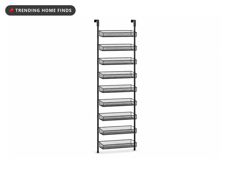 Black nine-tier over-the-door pantry rack mounted on a white door, filled with spice jars, packets and cleaning bottles
