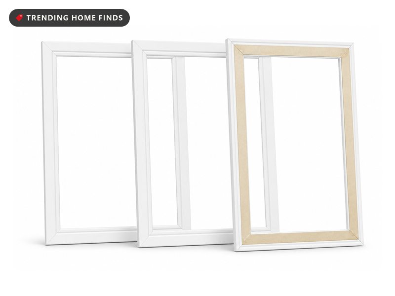 A pale bedroom wall half finished with white peel and stick picture frame moulding, a plain level and a paint roller resting on the floor below it.