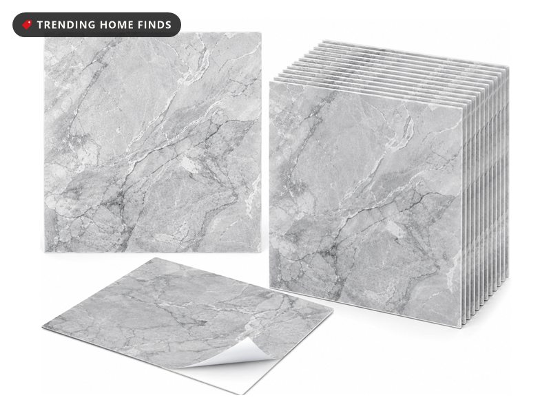 Stack of grey marble-look 12 inch square peel and stick vinyl backsplash tiles, one with its backing partly peeled away