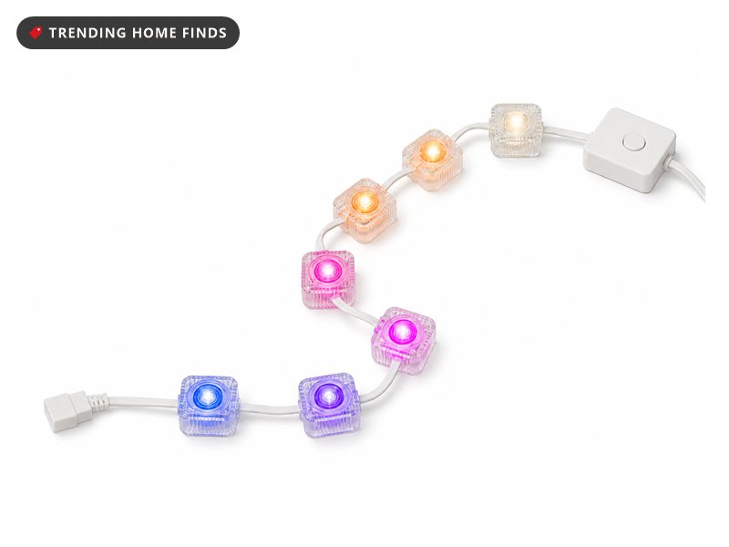 A run of small clear square light modules on one flat white cable, lit in warm white, orange, magenta, purple and blue.