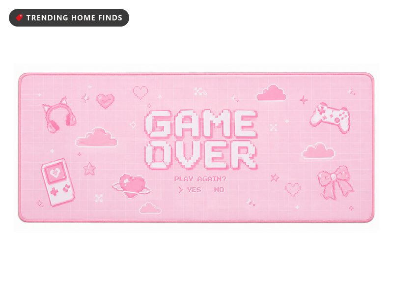 Wide pink desk mat printed in pixel art with the words GAME OVER and PLAY AGAIN YES NO, surrounded by a handheld console, a controller, headphones, hearts, clouds and a bow, with a stitched border