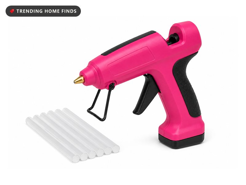 Hot pink cordless glue gun with a black rubber grip, brass nozzle and a fold-down wire stand, beside clear glue sticks.